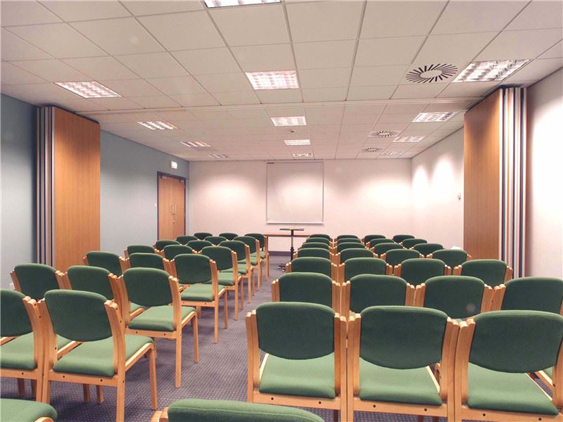 Wooden movable folding partition wall stacked neatly in an office training room with green chairs Wooden movable folding partition wall stacked neatly in an office training room with green chairs