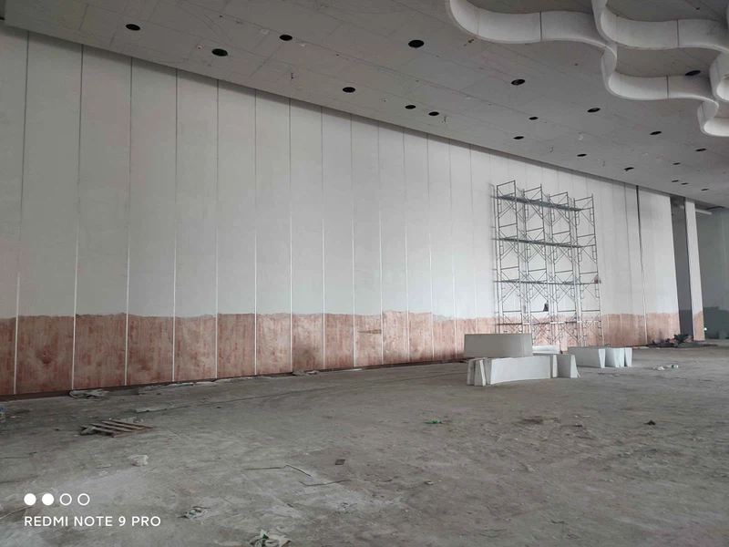 Installation of acoustic sliding wall divider in convention center showing plywood finish and sound barrier infill. Installation of acoustic sliding wall divider in convention center showing plywood finish and sound barrier infill.